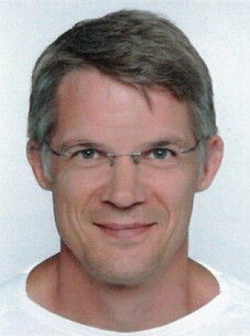 Björn Trauzettel mit Brille und kurzem Haar, neutraler Hintergrund.